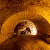 Superato il portale a destra si apre un primo ambiente, l�unico orientato in maniera obliqua rispetto ai tunnel. Al suo interno colpiscono subito delle massicce arcate in tufo che sostengono la volta